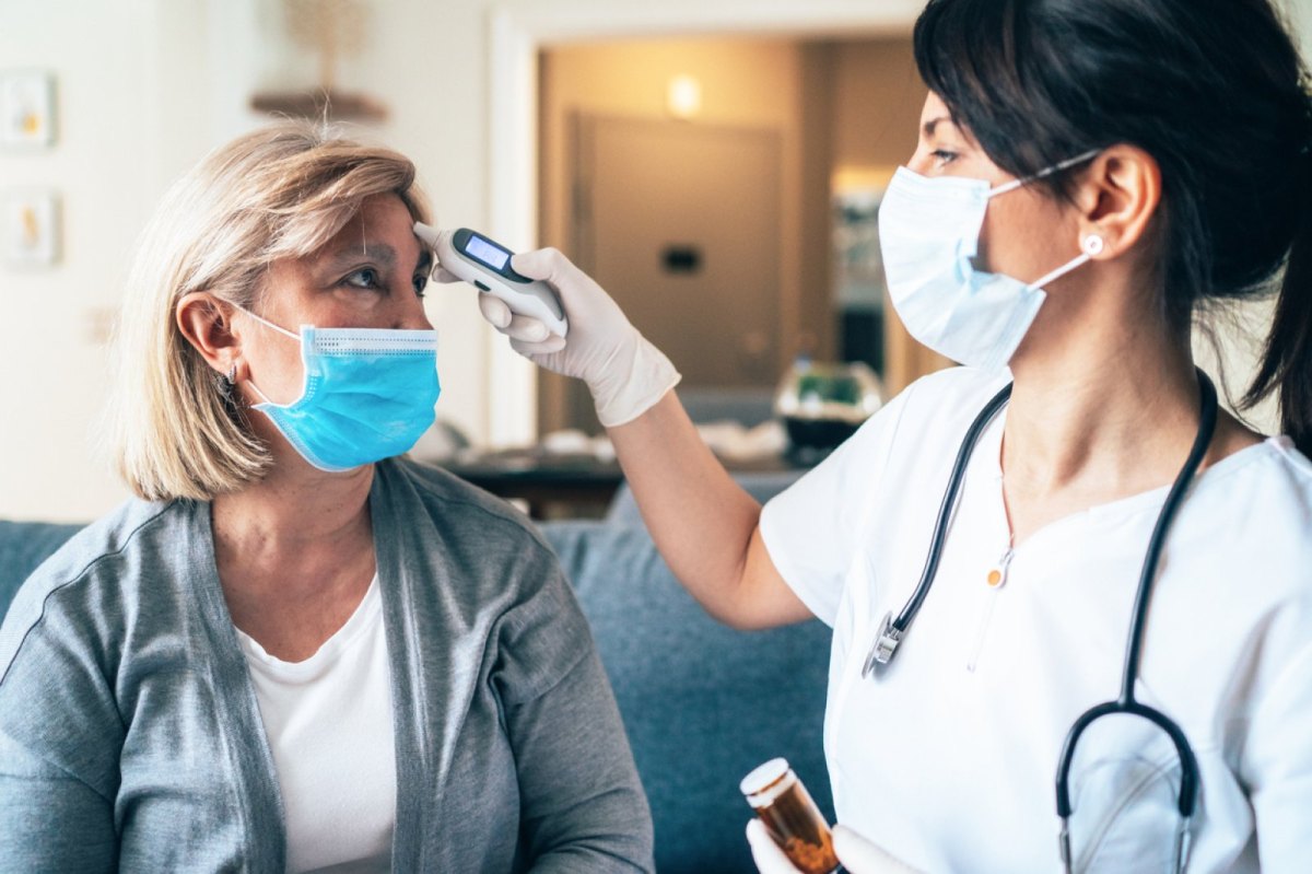 Ärztin mit Mundschutz misst Fieber bei einer Patientin an der Stirn.