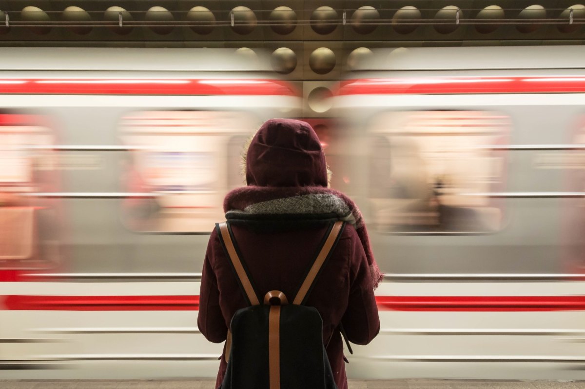 Eine junge Frau steht mit dem Rücken zum Betrachter am Bahnsteig