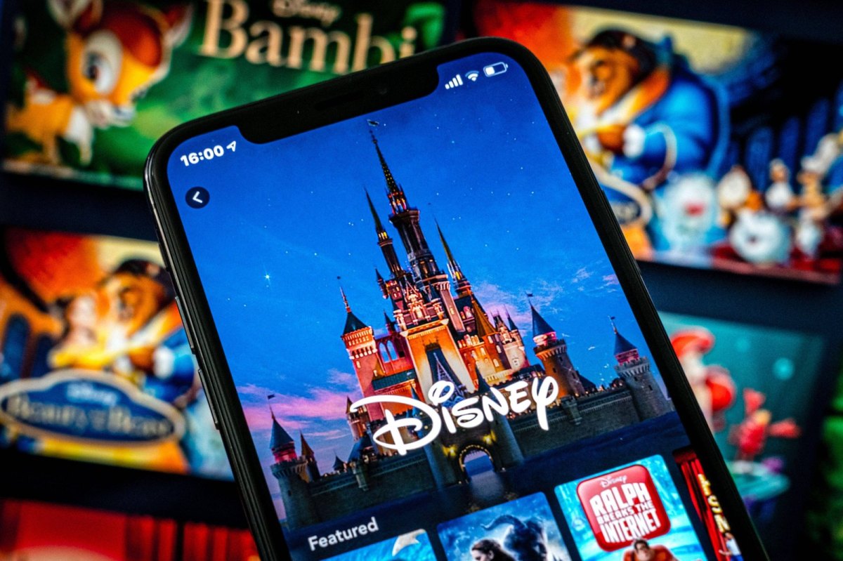 Handy mit dem Disney-Logo und dem Disney-Schloss. Im Hintergrund verschwommen: Filmcover von Bambi