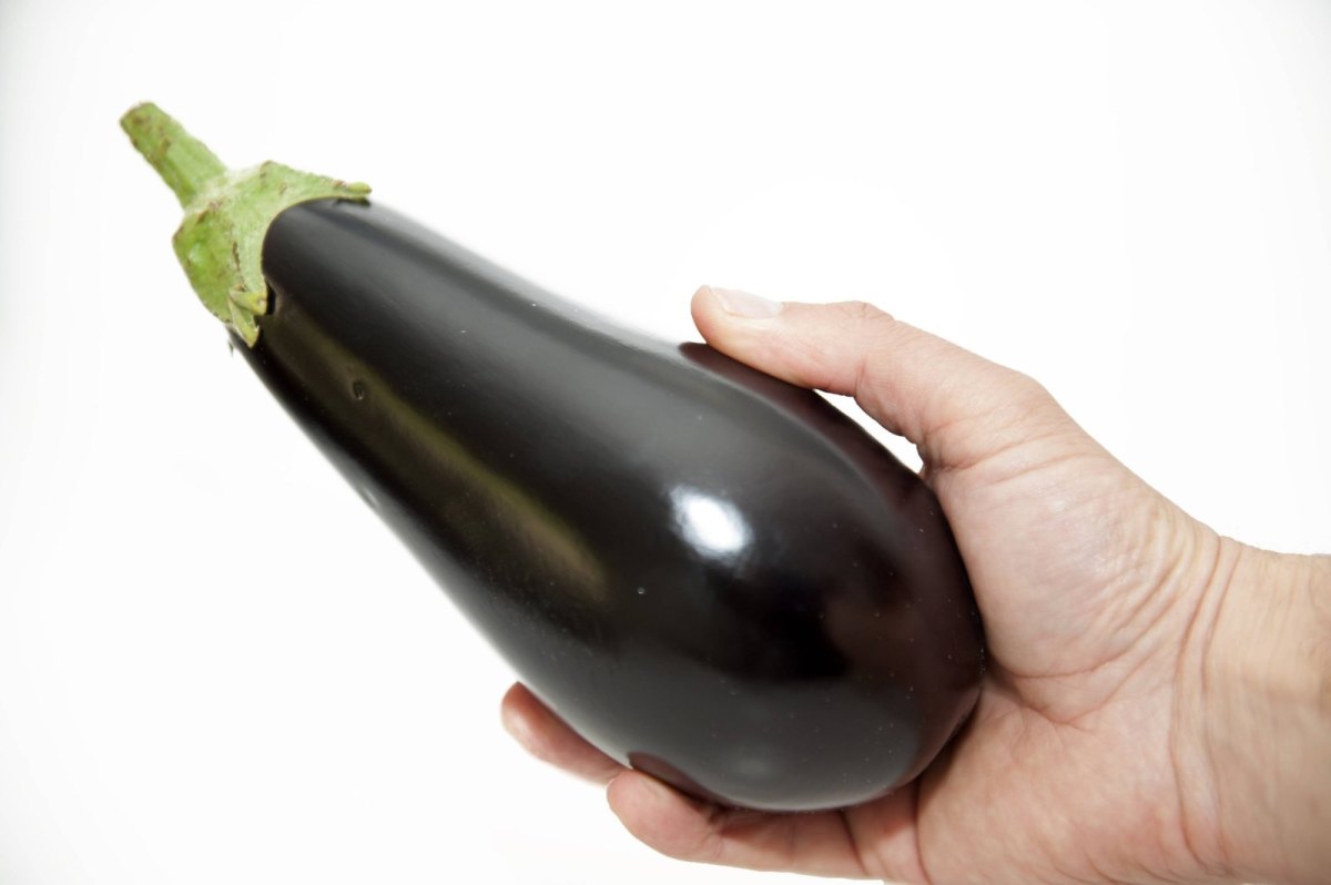 Eine Mann hält eine Aubergine in der Hand.