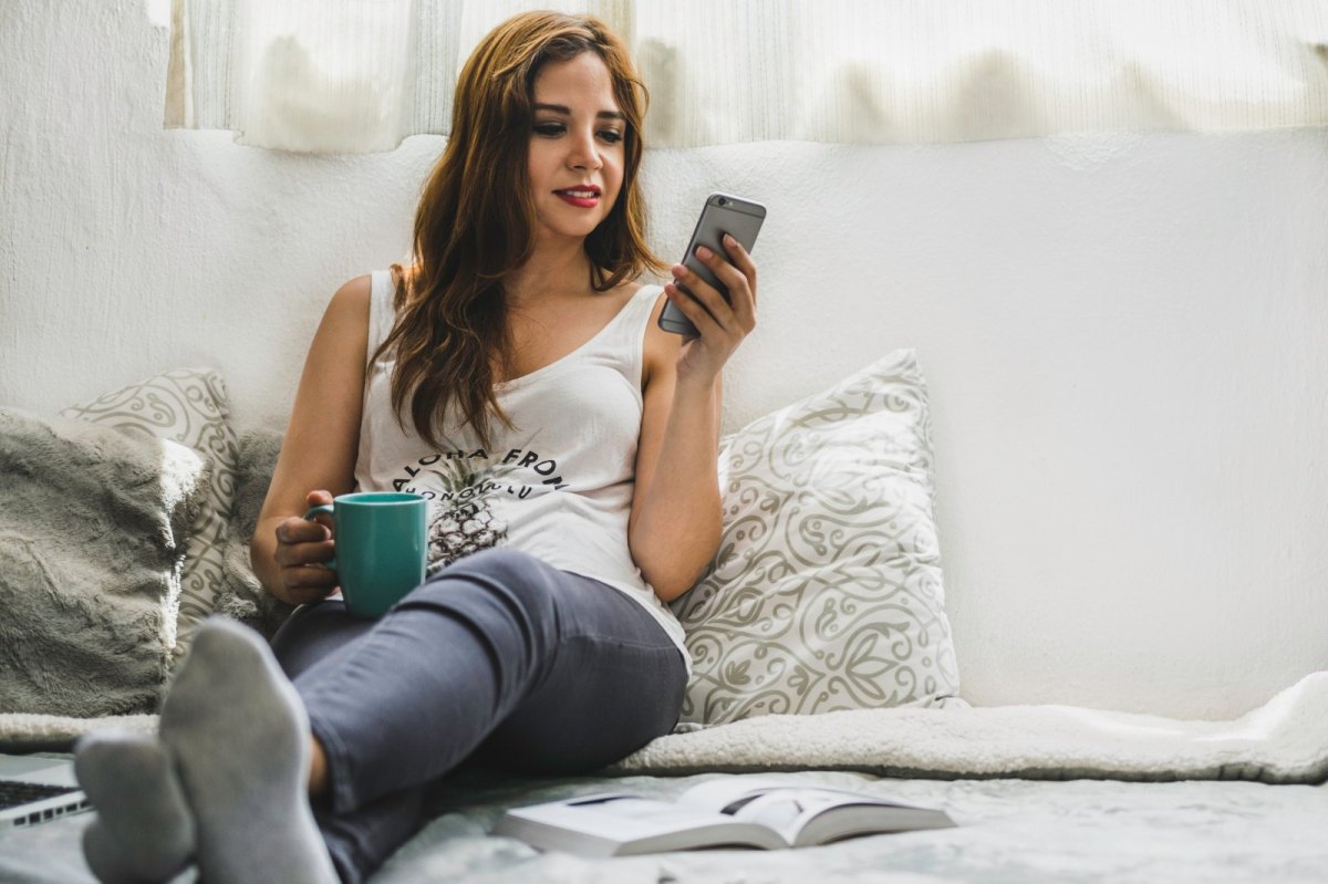 Eine Frau sitzt mit ihrem Handy auf dem Bett.