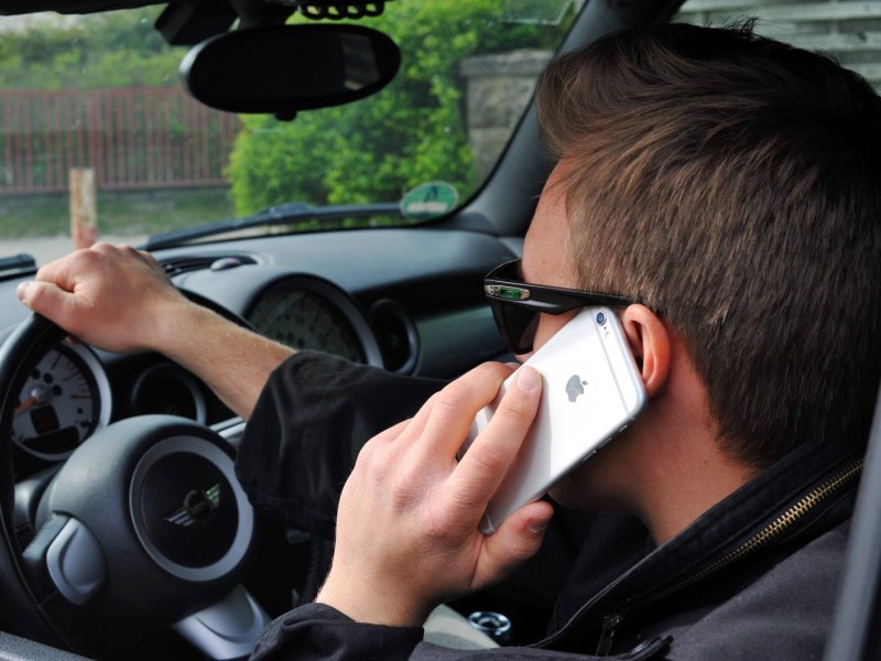 Mann mit Sonnenbrille telefoniert beim Autofahren mit seinem Handy.