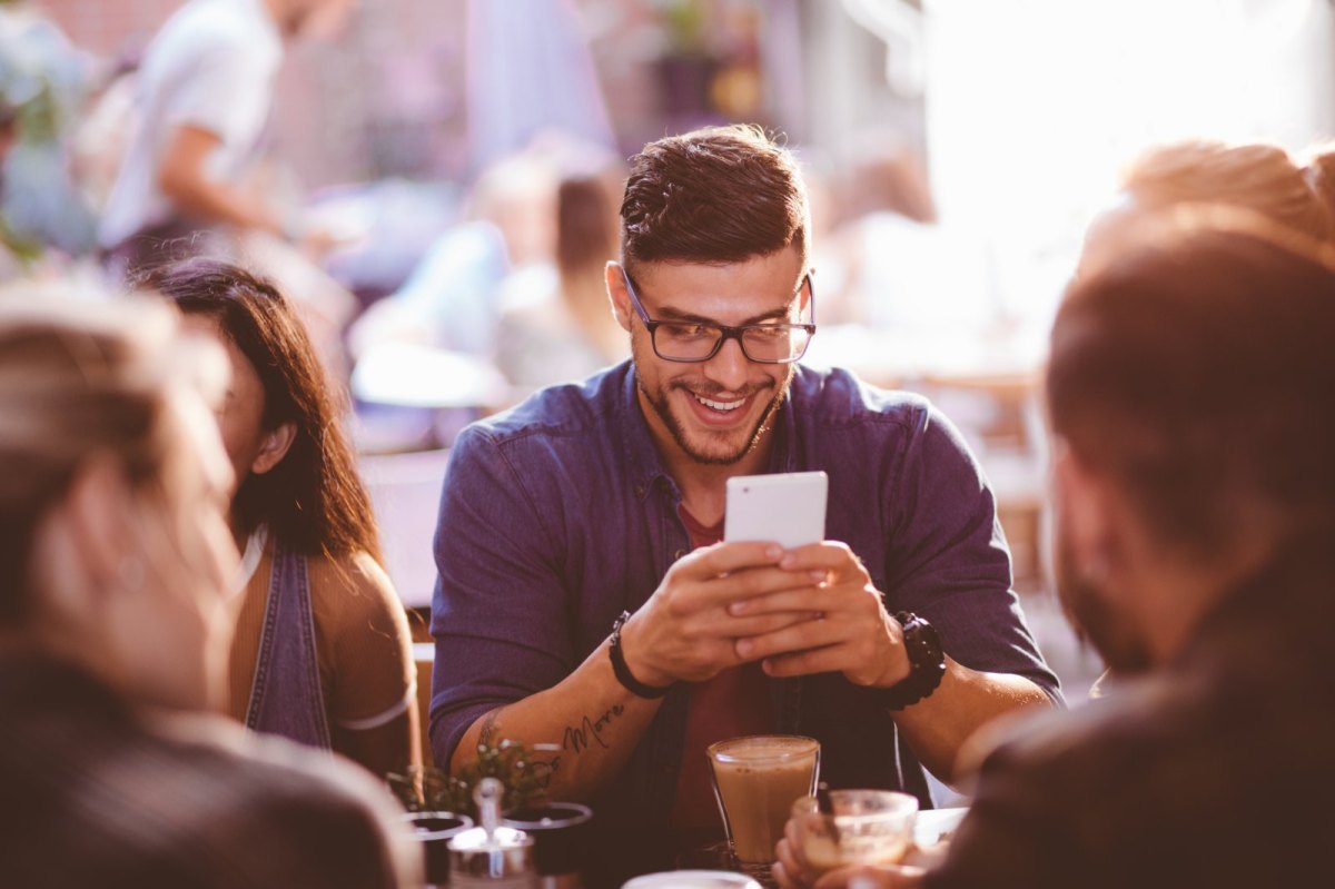 Mann sitzt im Café und schaut lachend auf sein Handy.