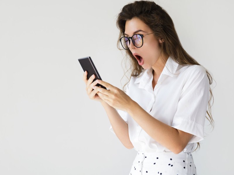 Frau mit Brille guckt geschockt auf ihr Handy.