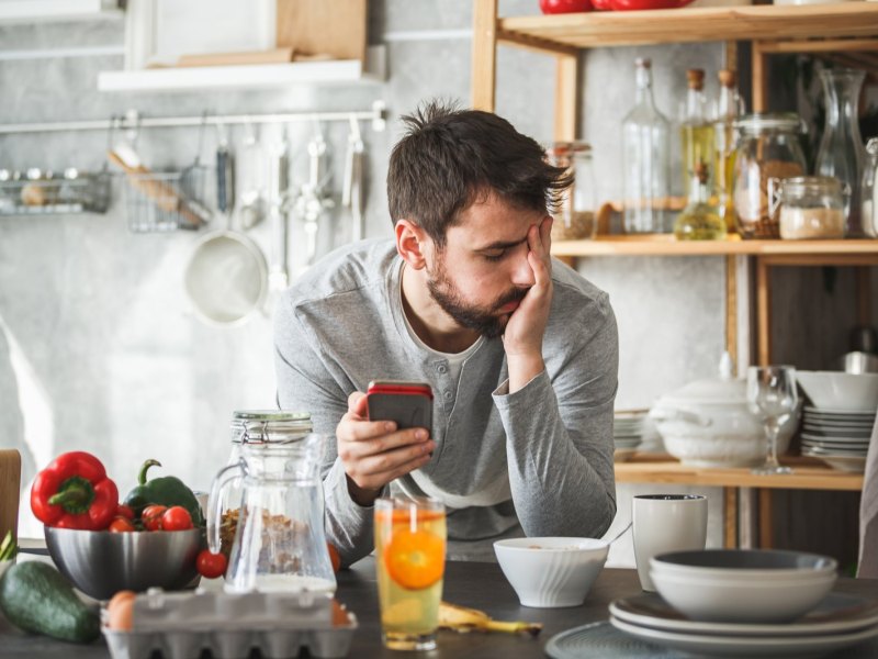 Mann genervt mit Handy in seiner Küche.