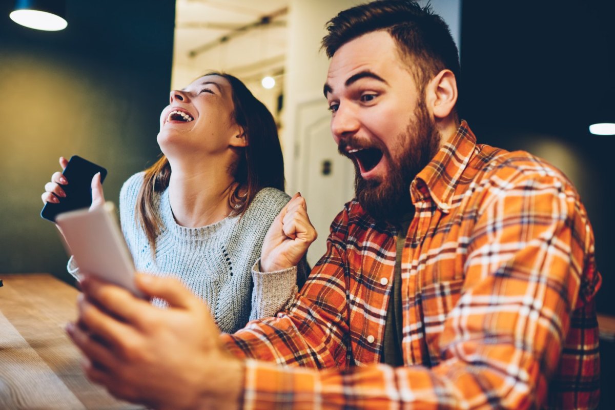 Mann und Frau schauen auf Handy und freuen sich sehr.