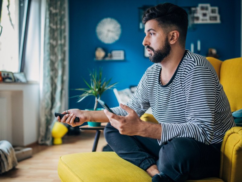 Mann hält Fernbedienung und Handy in der Hand.