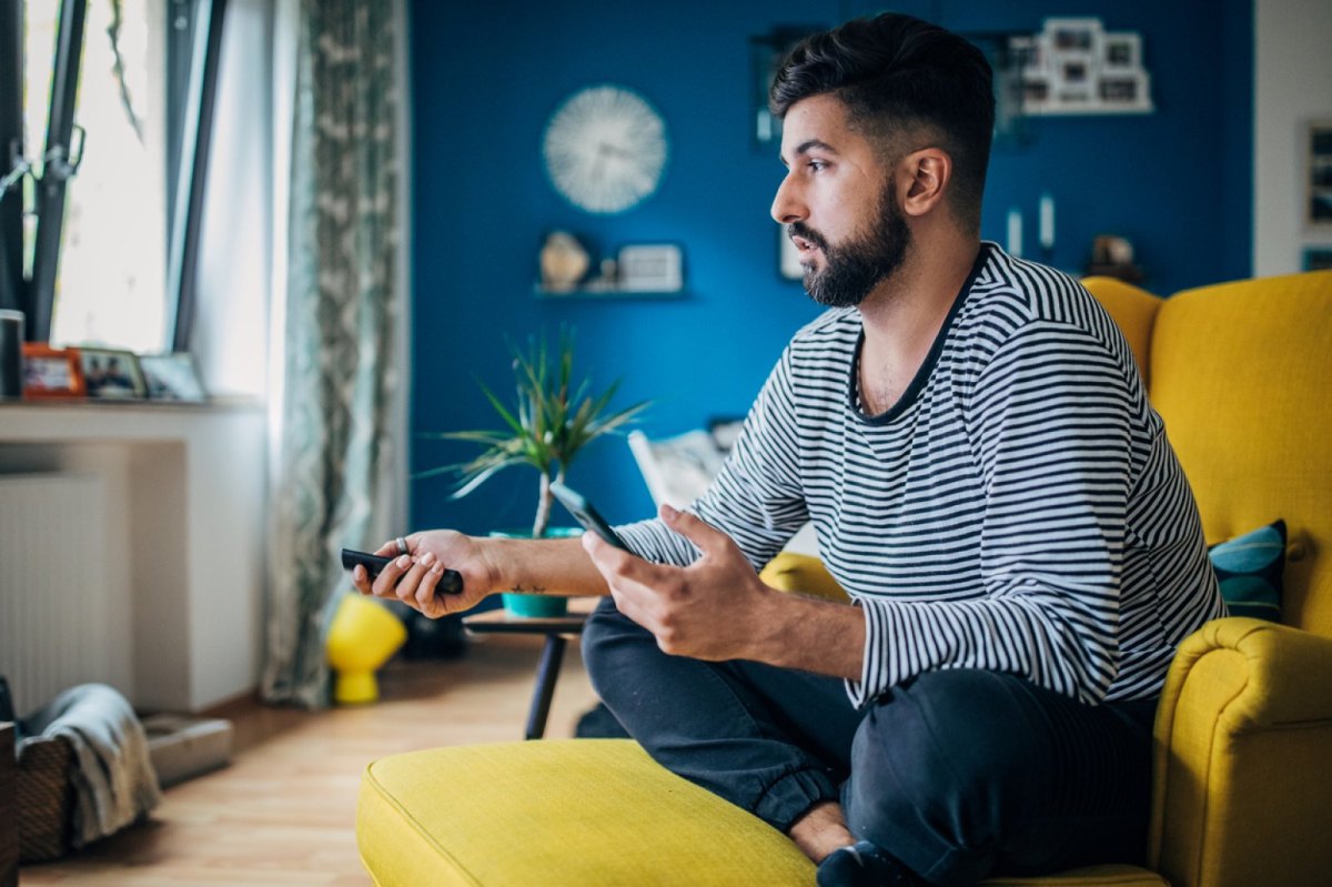 Mann hält Fernbedienung und Handy in der Hand.