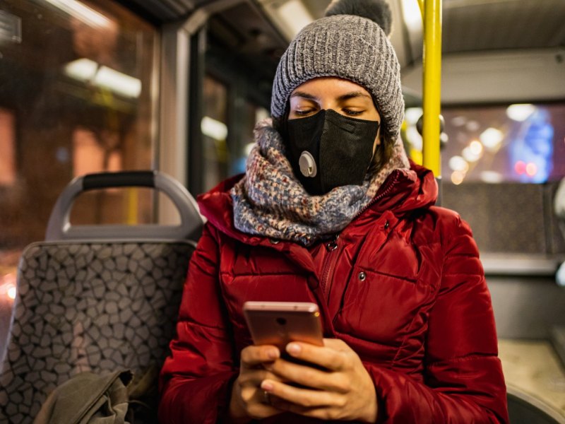 Frau mit Winterbekleidung und Maske im Bus.