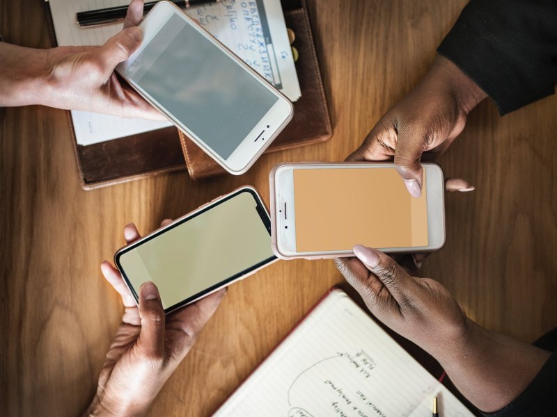 Drei Smartphones werden über einem Tisch mit Dokumenten drauf in den Händen gehalten.