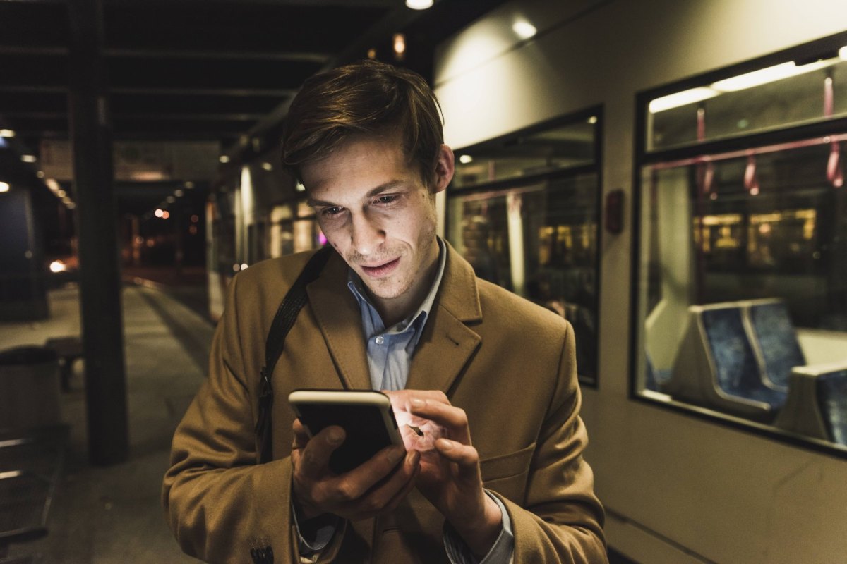 Mann schaut neben einer Straßenbahn auf sein Smartphone