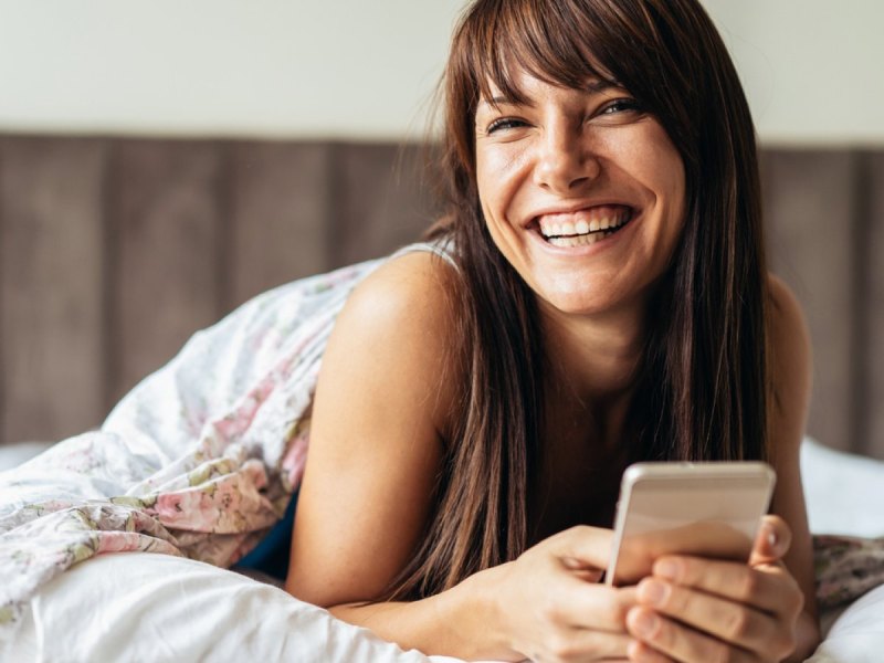 Frau mit Handy in der Hand im Bett.