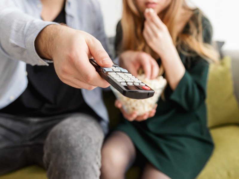 Paar sitzt mit Popcorn und Fernbedienung vor dem Fernseher