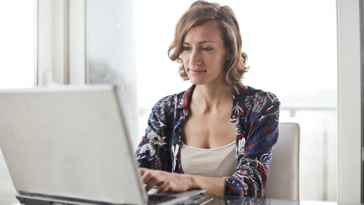 Eine Frau sitzt ein einem Tisch vor einem aufgeklappten Laptop.