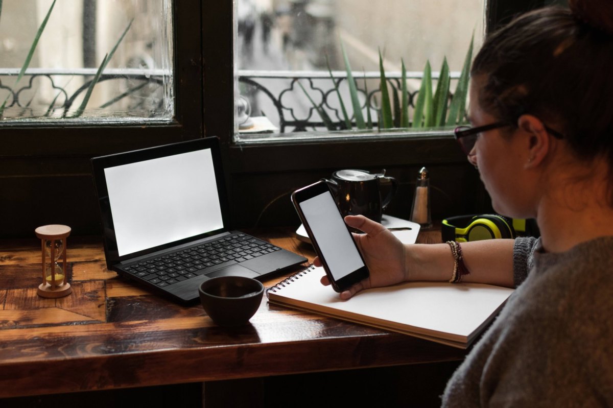 Frau sitzt vor Laptop mit Handy in der Hand