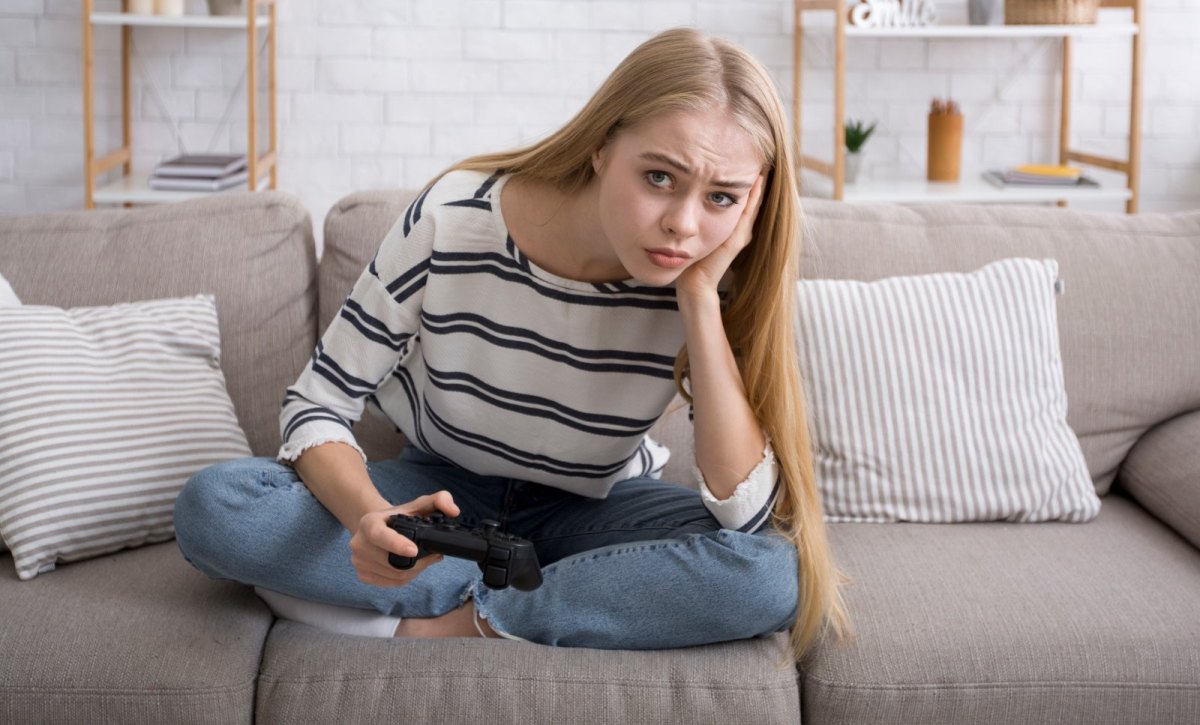 Eine junge Frau blickt mit einem Controller in der Hand skeptisch drein.