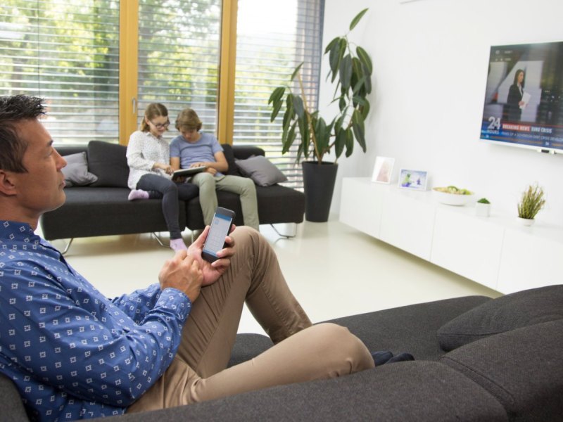 Mann mit Handy sitzt vor Fernseher.