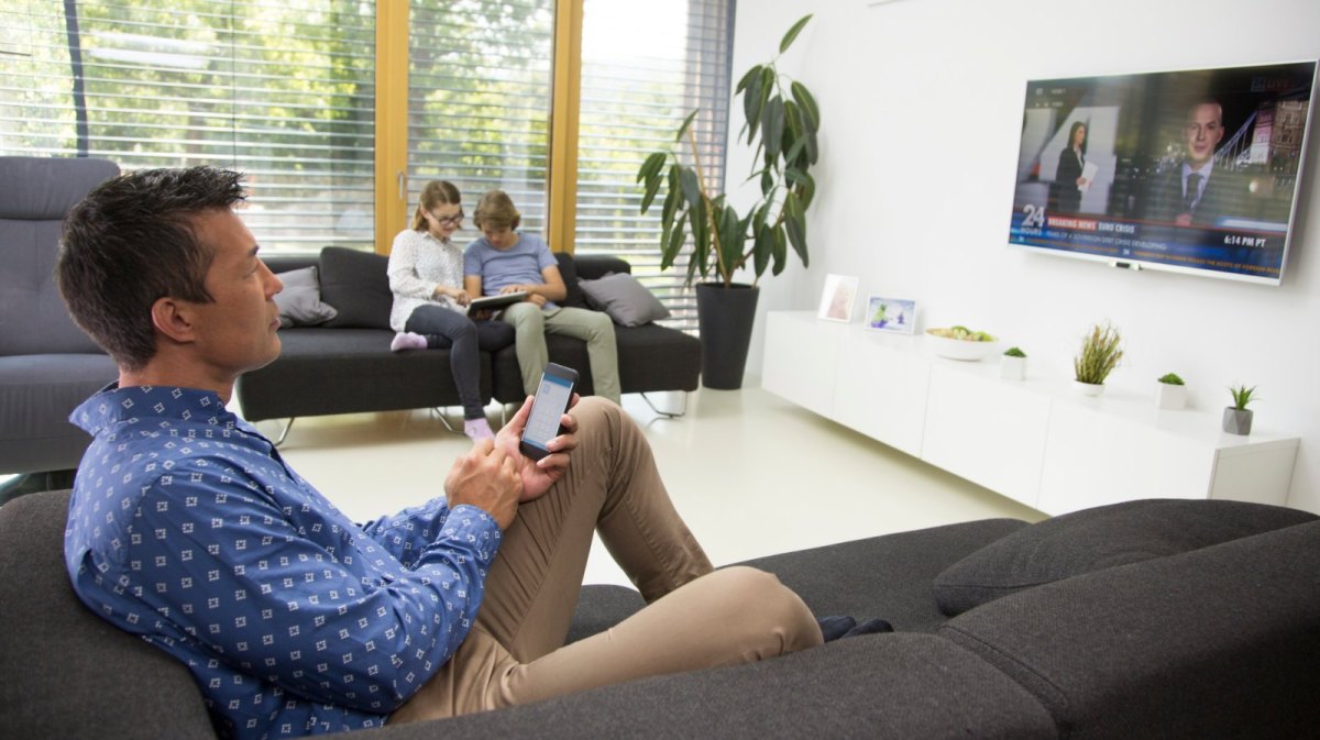 Mann mit Handy sitzt vor Fernseher.