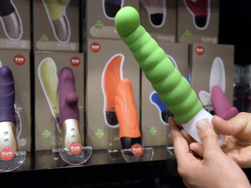 Hände halten grünen Vibrator in der Hand mit anderen Vibratoren im Hintergrund