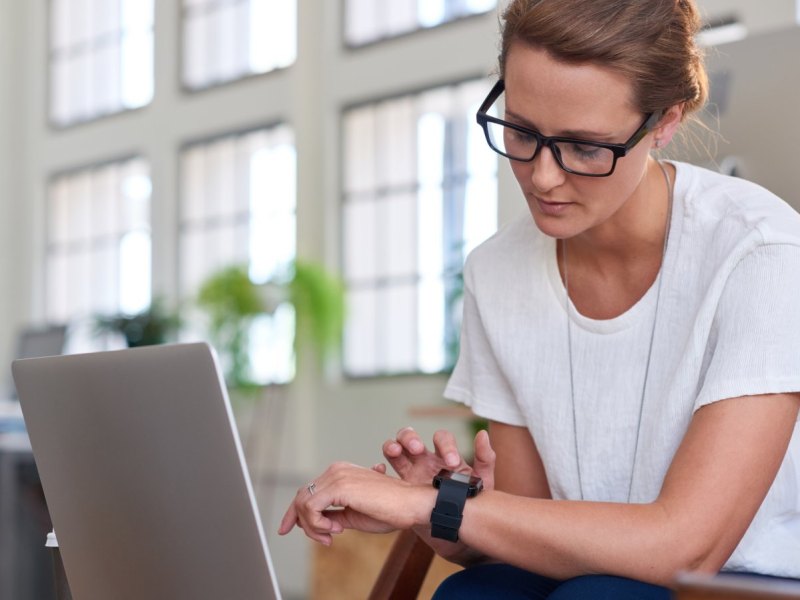 Frau mit Smartwatch vor Laptop.