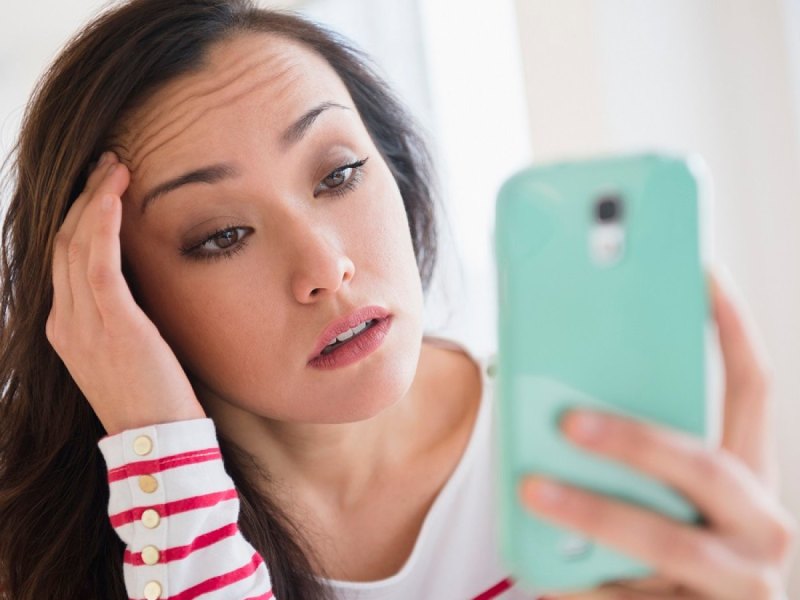 Frau schaut genervt/böse auf ihr Handy.