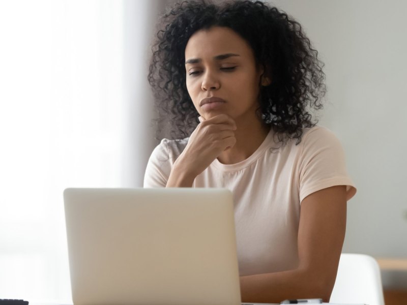 Frau sieht nachdenklich auf ihren Laptop.