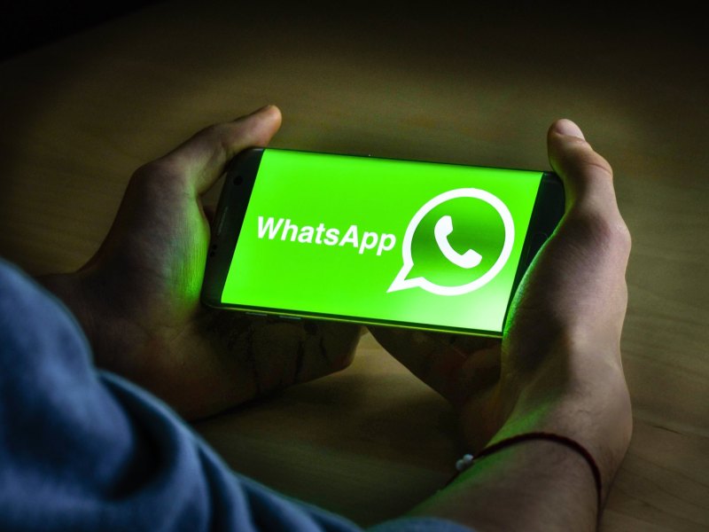 Mann hält Handy mit WhatsApp-Logo auf Display in den Händen.