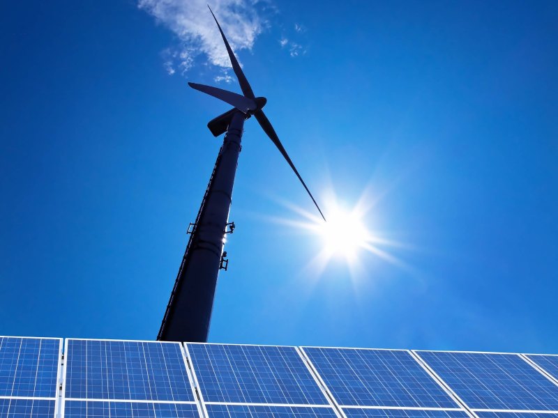 Windrad vor blauem Himmel und Sonne mit Solarpanelen am Boden