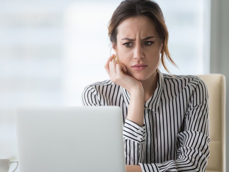 Frau sieht genervt auf ihren Laptop.