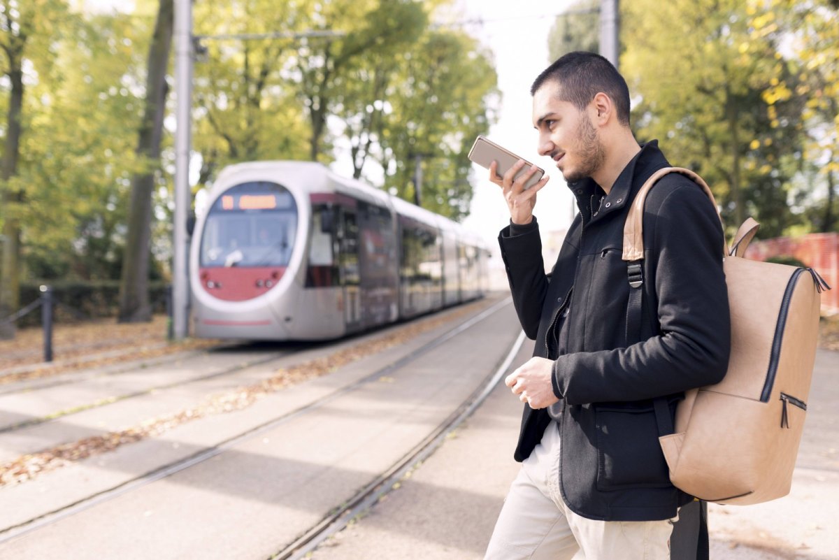 Mann spricht in Smartphone während er bei herannahendem Zug über die Gleise läuft