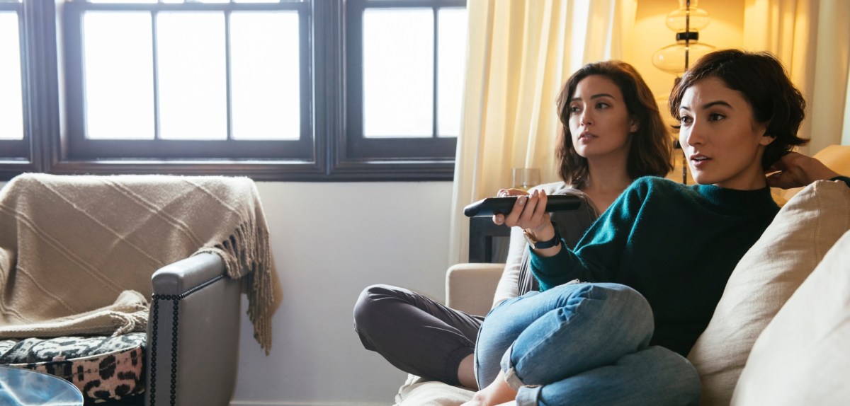 Zwei junge Frauen sitzen auf dem Sofa und schauen Fernsehen