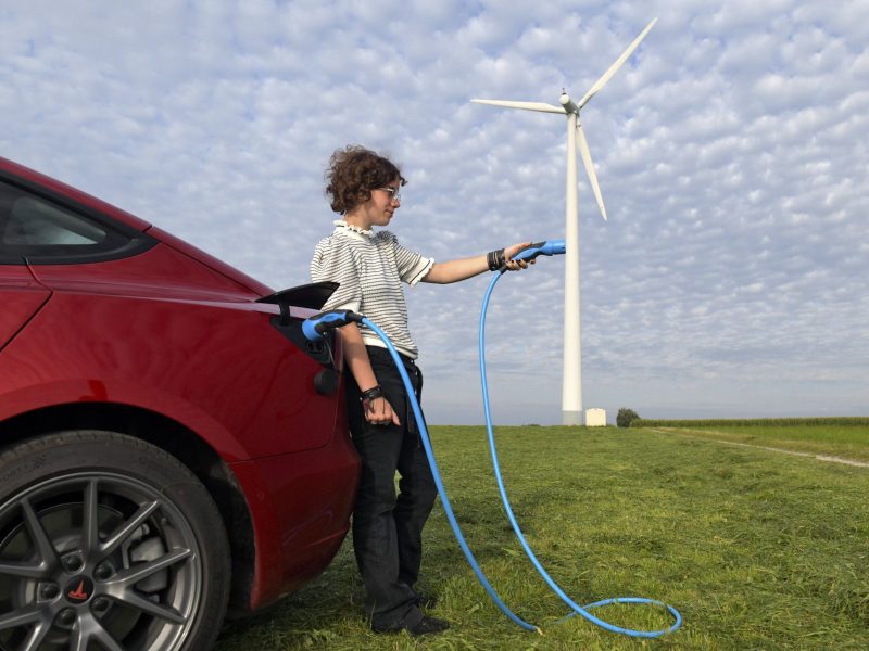 Frau mit Ladekabel von Elektroauto an Windrad