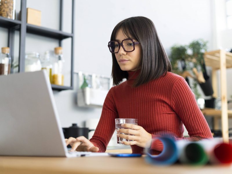 Frau sitzt mit Tasse vor Laptop