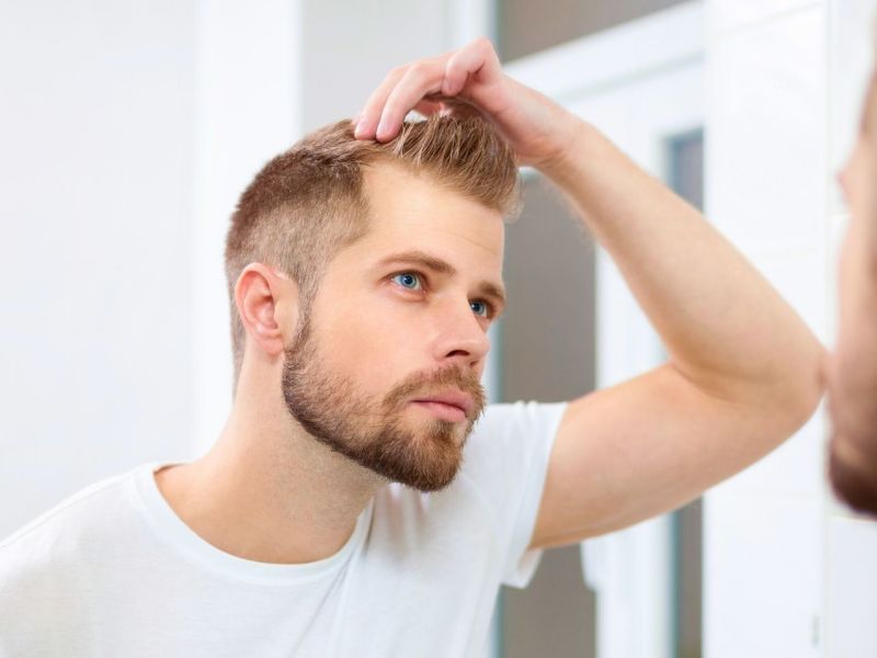 Mann begutachtet seine Haare vor dem Spiegel.