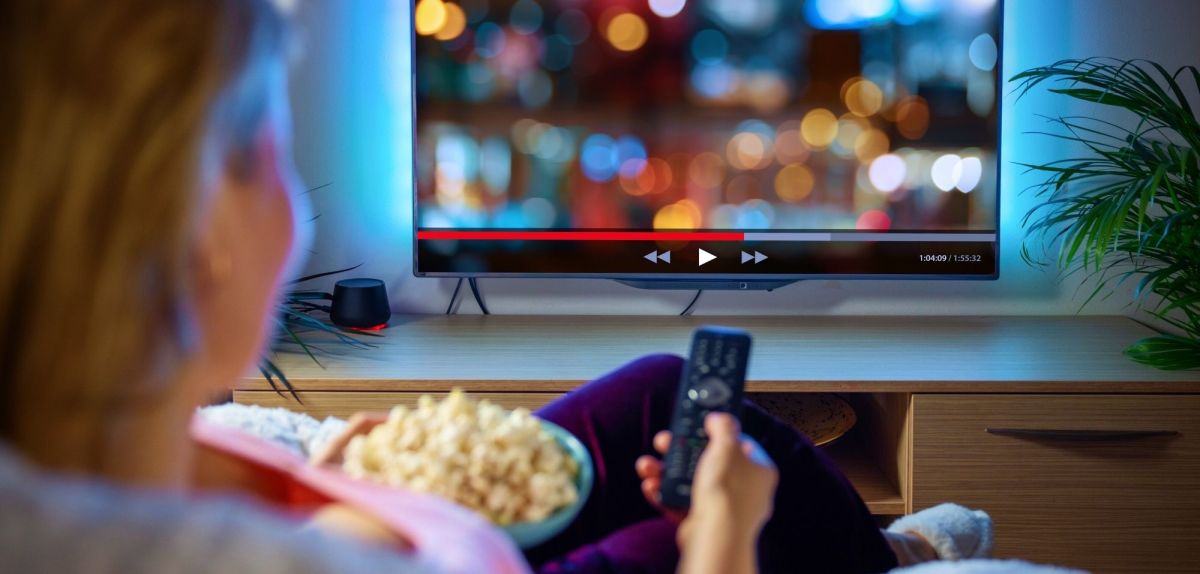 Frau sitzt vor dem Fernseher mit einer SchÃ¼ssel Popcorn und streamt.