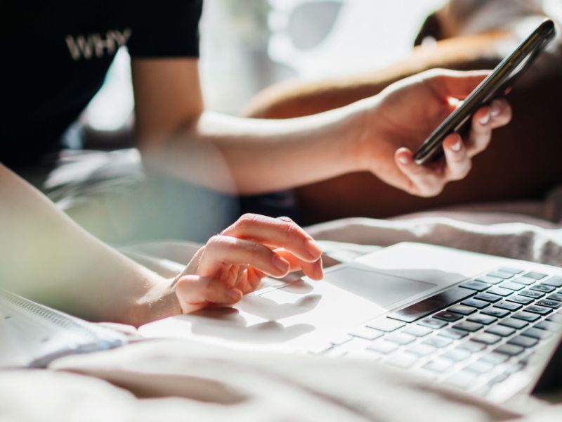 Person an Laptop und Handy gleichzeitig