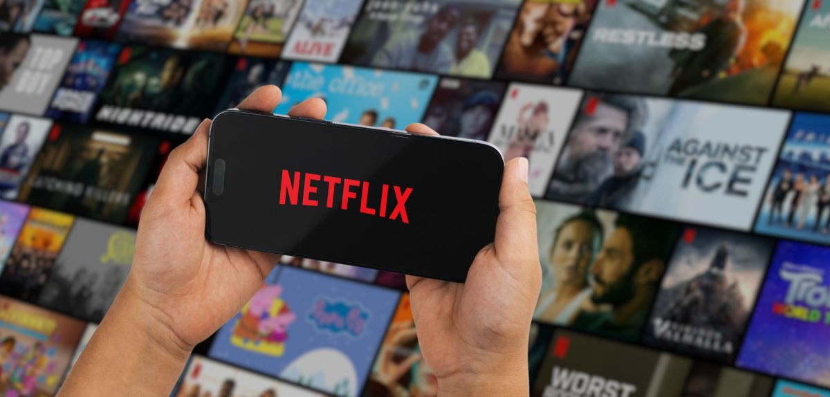 Netflix-Logo auf einem Handy-Display, im Hintergrund viele Kacheln von Filmen und Serien.