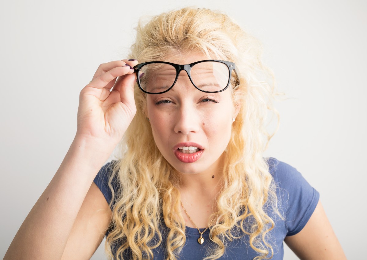 Frau hebt Brille und kneift die Augen zusammen