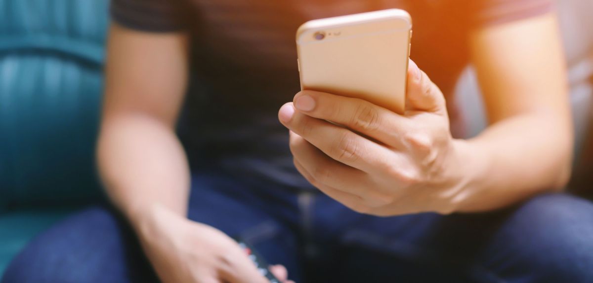 Mann mit Fernbedienung und Smartphone in der Hand