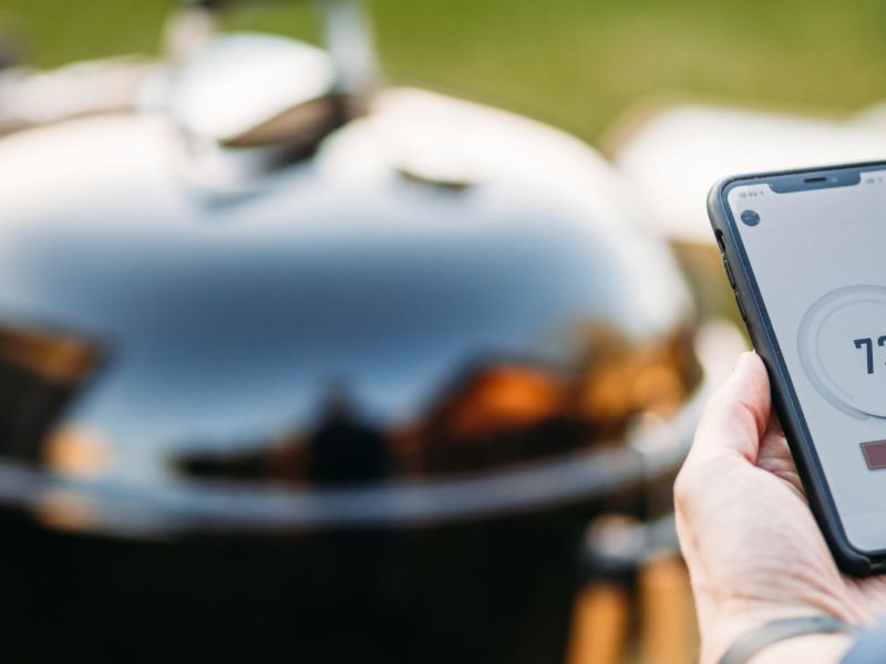 Person mit Smartphone in der Hand vor einem Grill