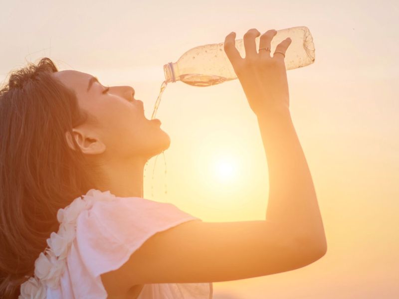 Frau lässt Wasser aus einer Flasche in ihren Mund laufen