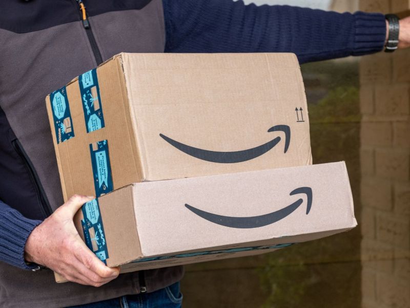 Bote mit einem Stapel Amazon-Pakete klingelt an einer Haustür.