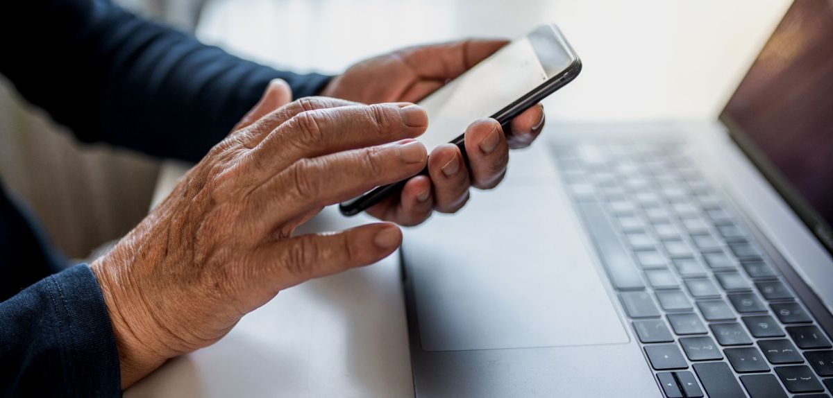 Alte Person nutzt ein Smartphone vor einem Handy.