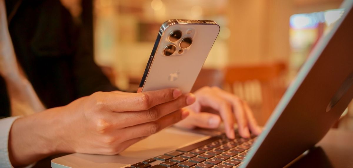 Person hält ein iPhone 14 Pro in der Hand an einem Laptop sitzend.