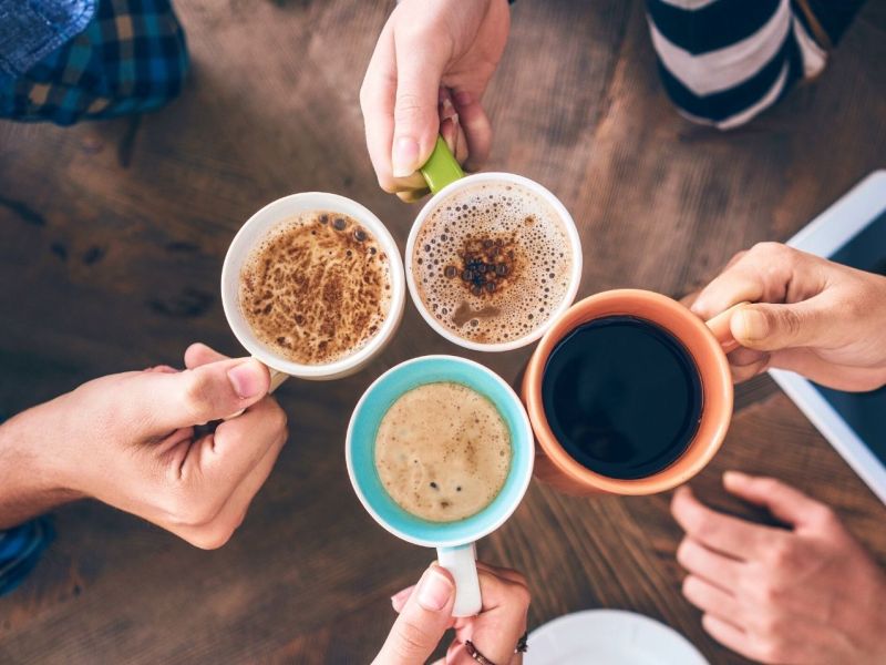 Mehrere Personen halten ihre Tassen mit Kaffee in die Mitte.