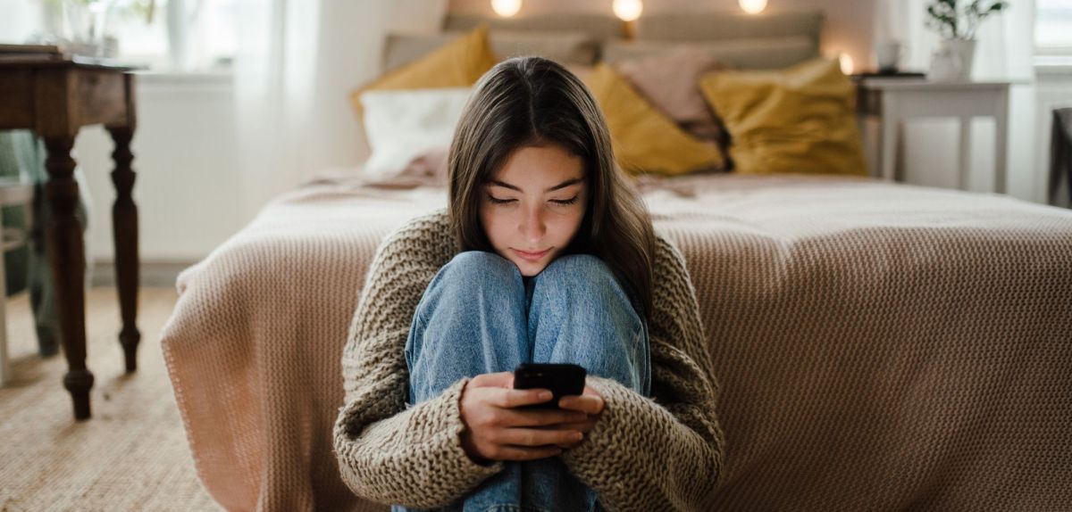 Mädchen sitzt Zuhause auf dem Boden an ihrem Handy.