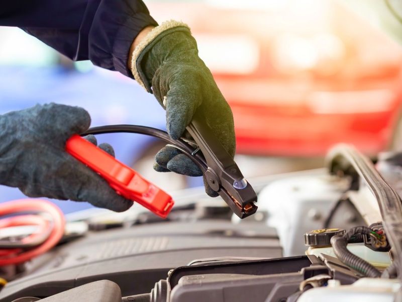 Hände helfen Starthilfekabel über einer Autobatterie