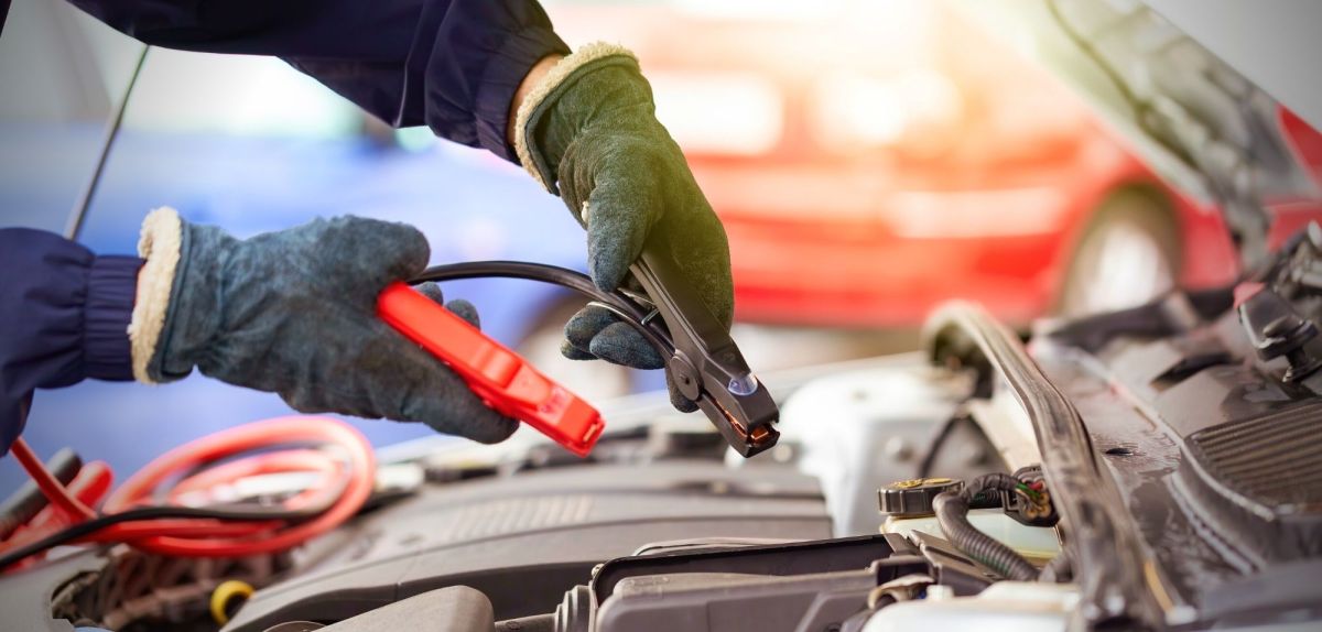 Hände helfen Starthilfekabel über einer Autobatterie