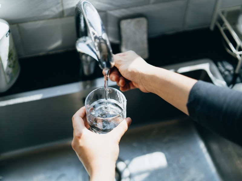 Frau gießt Wasser aus dem Hahn in ein Glas