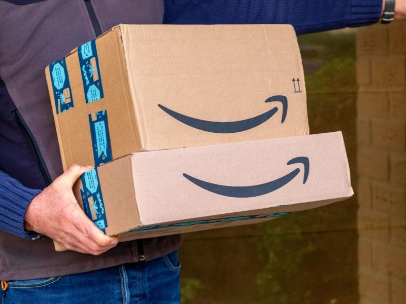 Mann hält Stapel Pakete von Amazon in der Hand.